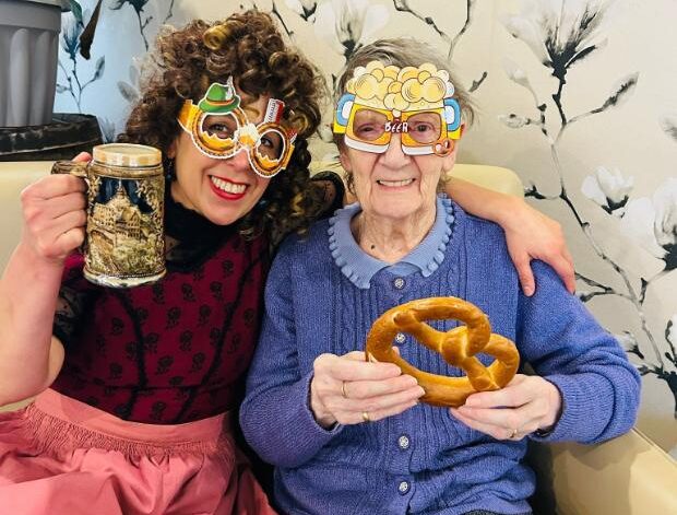 resident holding a pretzel and a staff member in dress up for oktoberfest