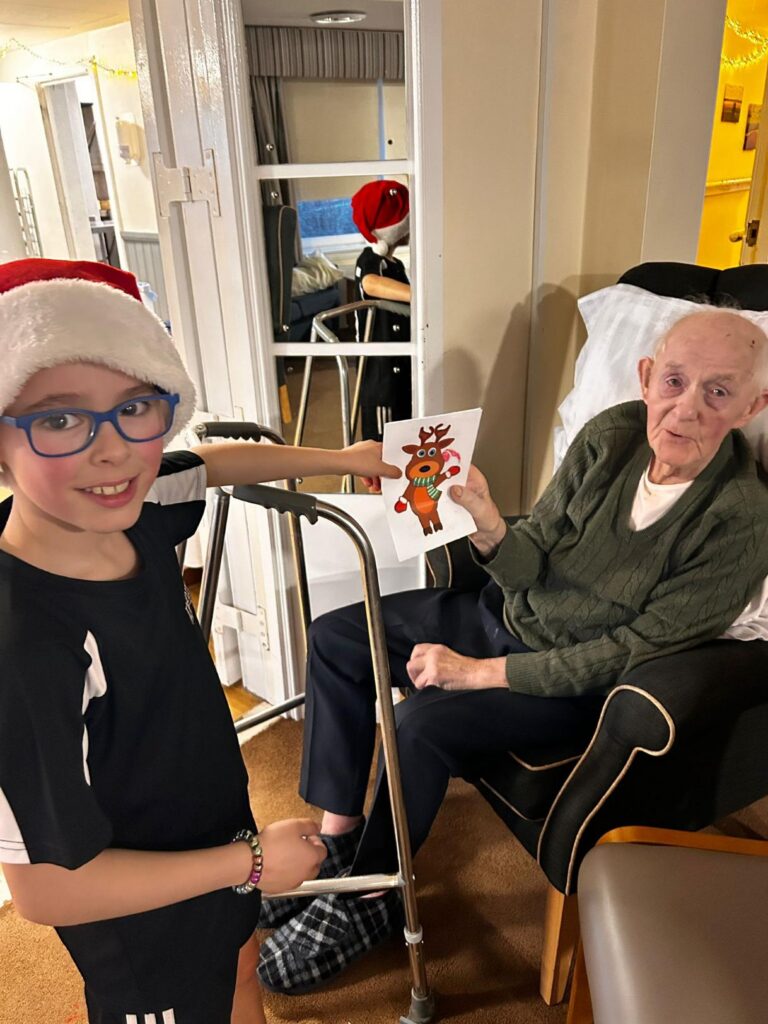 child smiles while handing a homemade christmas card to elderly man
