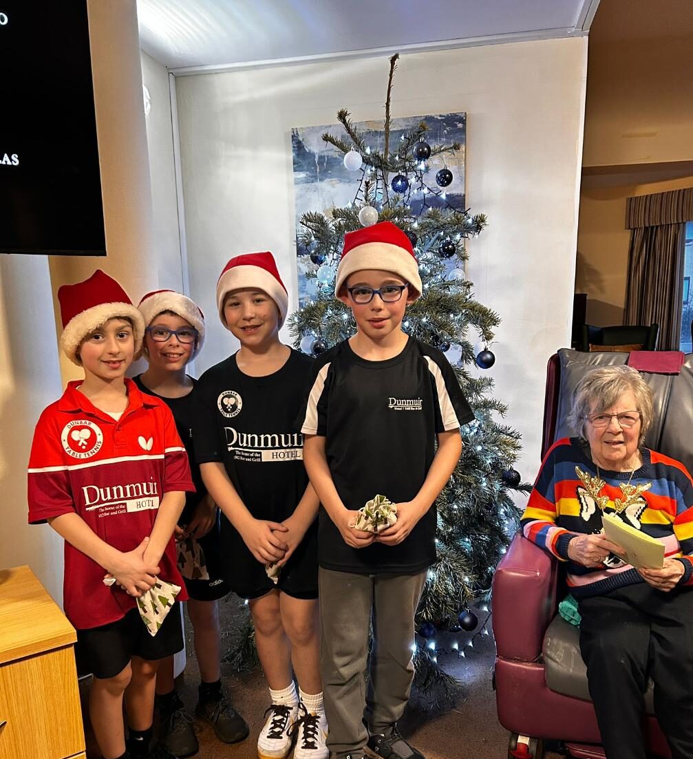 children standing with care home resident in front of christmas tree