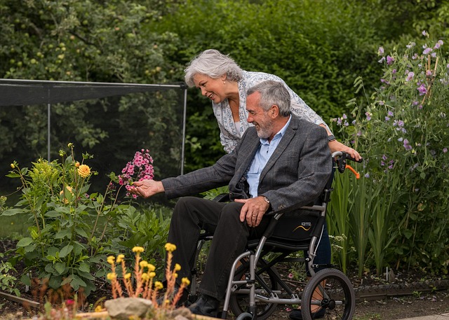 woman pushing elderly man in wheelchair though care home garden